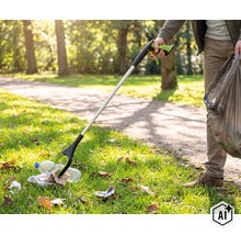 Person använder en plocktång i en park för att plocka upp en plastflaska från marken och lägga den i en soppåse. (Image AI modified or generated)