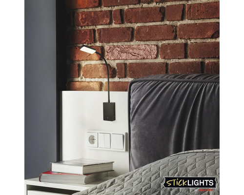 Modern LED vägglampa med flexibel arm som läslampa vid sängen framför en tegelvägg.