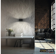 Modern rektangulär vägglampa med ljuskäglor uppåt och nedåt på en strukturerad vägg i vardagsrummet. Sticklights logotyp.