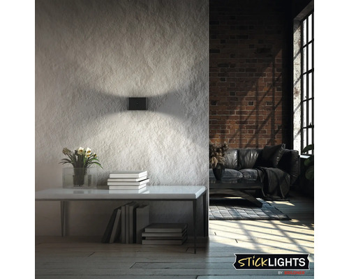 Modern rektangulär vägglampa med ljuskäglor uppåt och nedåt på en strukturerad vägg i vardagsrummet. Sticklights logotyp.