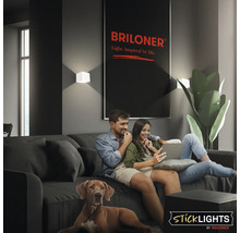 Ett par sitter i en soffa med sin hund i ett modernt vardagsrum med Briloner-vägglampor och en Briloner-logotyp.