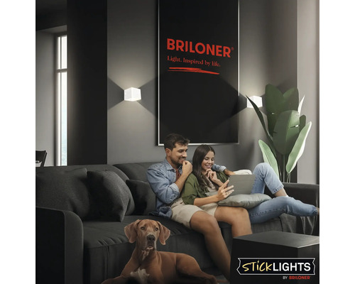 Ett par sitter i en soffa med sin hund i ett modernt vardagsrum med Briloner-vägglampor och en Briloner-logotyp.