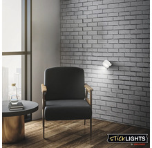 Vardagsrum med fåtölj vid en tegelvägg och en monterad självhäftande LED lampa Sticklights by Briloner