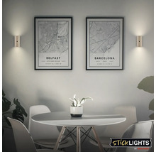 Två vägglampor lyser upp två inramade stadskartor över Belfast och Barcelona i en modern matplats. Sticklights logotyp.