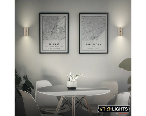 Två vägglampor lyser upp två inramade stadskartor över Belfast och Barcelona i en modern matplats. Sticklights logotyp.
