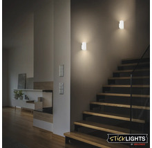 Två moderna vägglampor i ett vardagsrum med trappa och indirekt belysning i Briloner Sticklights logotypdesign.