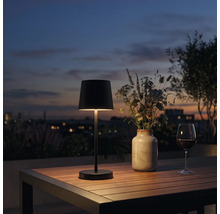 Modern LED bordslampa for utomhusbruk pa ett trabord med blomvas och vinglas i skymningen.