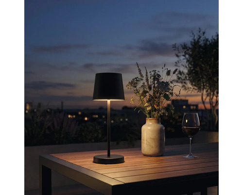 Modern LED bordslampa for utomhusbruk pa ett trabord med blomvas och vinglas i skymningen.