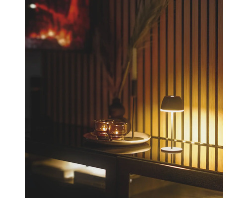 En liten bordslampa lyser bredvid värmeljus på en bricka framför en vägg med trälister.