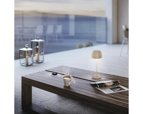 Modern LED bordslampa på ett träbord med en kaffekopp och en tidning på en terrass med havsutsikt.