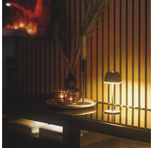 Modern uppladdningsbar bordslampa på en skänk framför en trälamellvägg med varm belysning och ljus på en dekorativ bricka.