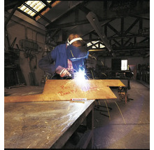 En svetsare bearbetar en metallplatta med en Edding märkpenna i en industriell verkstadsmiljö.
