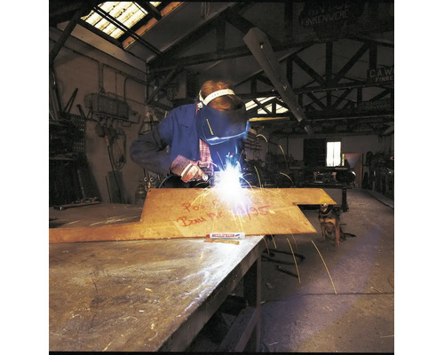 En svetsare bearbetar en metallplatta med en Edding märkpenna i en industriell verkstadsmiljö.