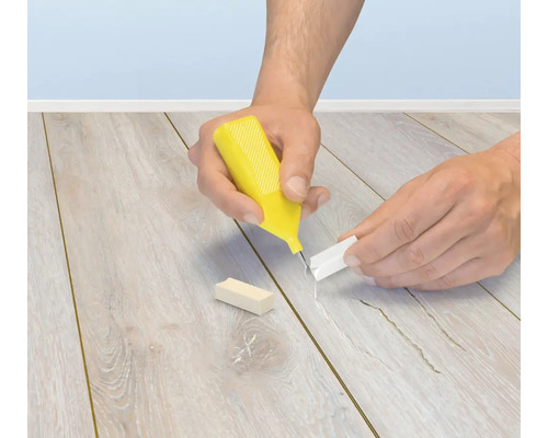 Person som anvander ett reparationsset for laminat och parkett for att laga fogar och repor i golvet