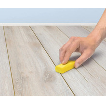 En hand använder en reparationsvaxstift för att laga repor på ett laminatgolv.