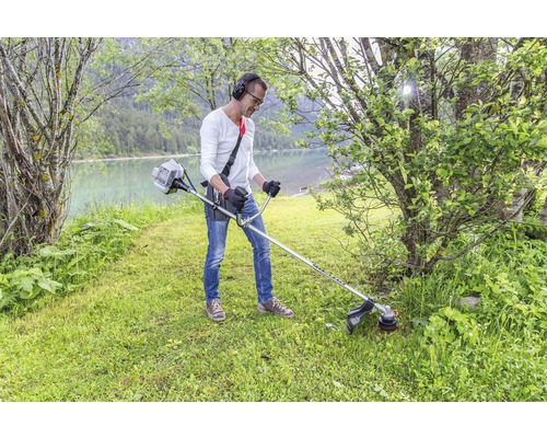 Man med hörlurar klipper gräs med en trimmer vid sjön