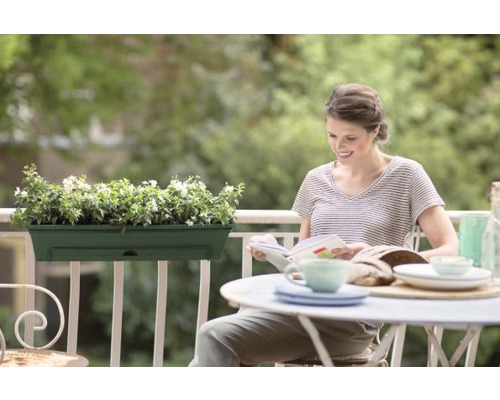 Kvinna läser på balkongen med blomlåda och dukat bord