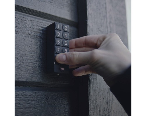 En hand använder ett Yale sifferlås på en dörr.