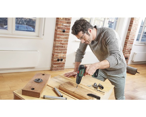 En man borrar ett hål i en träplanka med en borrmaskin.