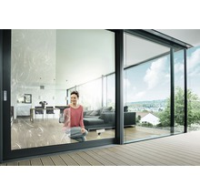 Kvinna putsar fönster i ett modernt vardagsrum med glasskjutdörrar och terrass.