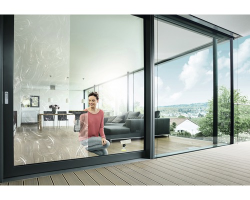 Kvinna putsar fönster i ett modernt vardagsrum med glasskjutdörrar och terrass.