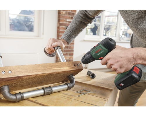 En person borrar ett hål i en träplanka med rörkopplingar med en sladdlös skruvdragare.