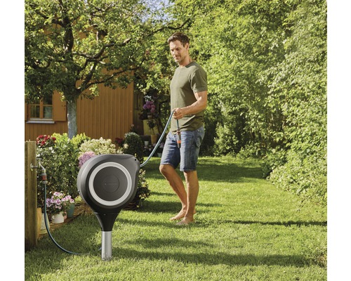 Trädgårdsscen med slangbox och en man som håller i en trädgårdsslang.