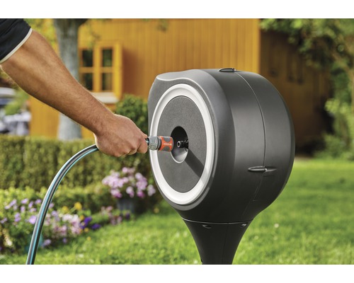 Trädgårdsscen med slangvinda på gräsmatta med blommor och trädgårdshus i bakgrunden