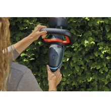 En person använder en Gardena batteridriven häcksax framför en häck.