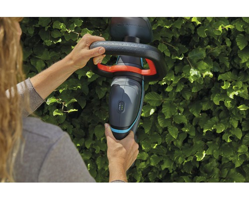En person använder en Gardena batteridriven häcksax framför en häck.