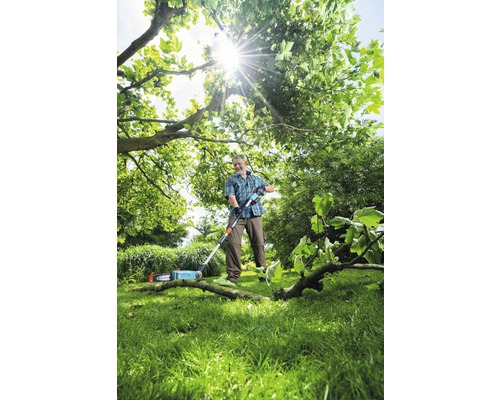 Man som beskär grenar med en stångsåg i en trädgård.