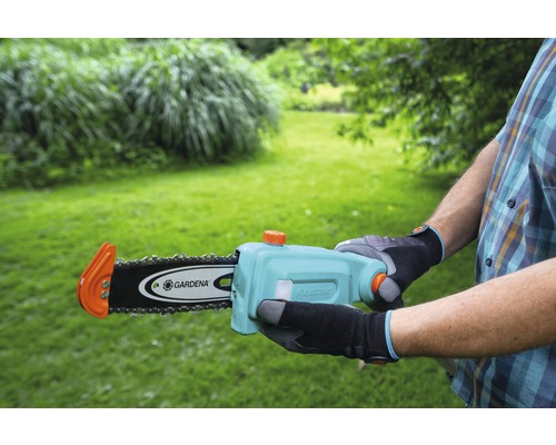 Person håller i en Gardena batteridriven motorsåg framför en trädgård