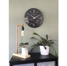 Svart väggklocka bredvid bordslampa och krukväxter på ett skåp