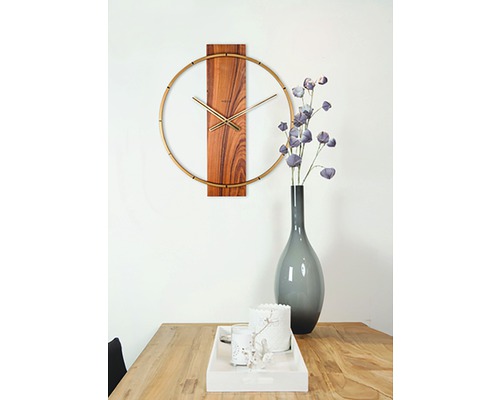 Väggklocka med trädetaljer och gyllene accenter ovanför ett träbord med dekorationer.