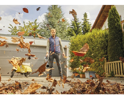 Man använder en lövblås för att ta bort löv på en gård.
