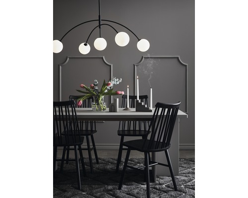 Matbord med stolar, blomvas, ljusstakar och hänglampa i en matsal.