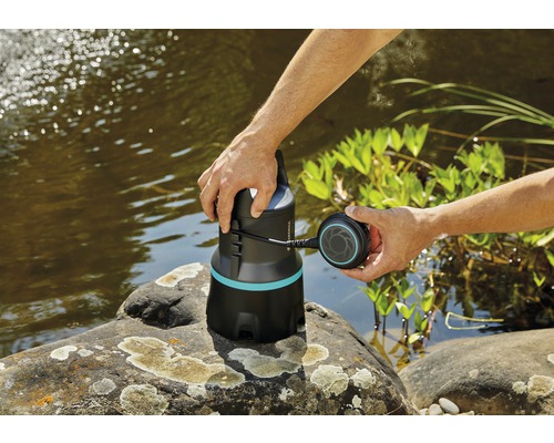 Trädgårdsvy med damm och dränkpump i handen