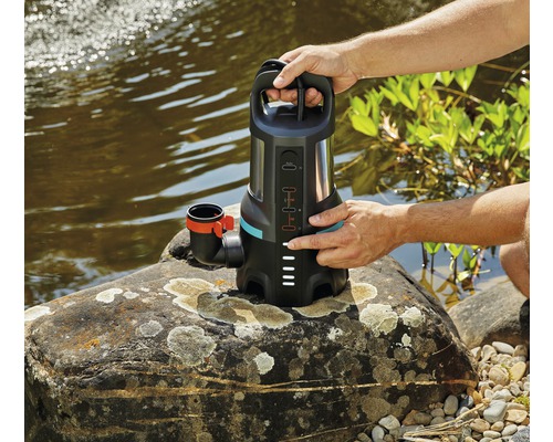 En person använder en Gardena smutsvattenpump vid stranden av ett vattendrag.