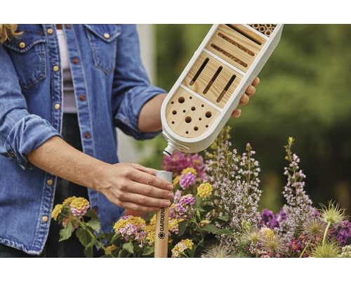 En person fäster ett Gardena insektshotell på en pinne i en trädgård.