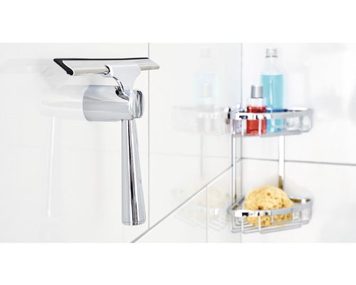 Duschskrapa av metall med hållare monterad på kakelvägg, med duschtillbehör i bakgrunden