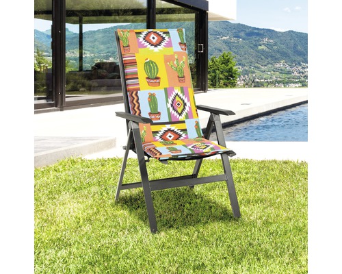 Trädgårdsstol med dyna i kaktusmönster på gräsmatta framför pool och hus