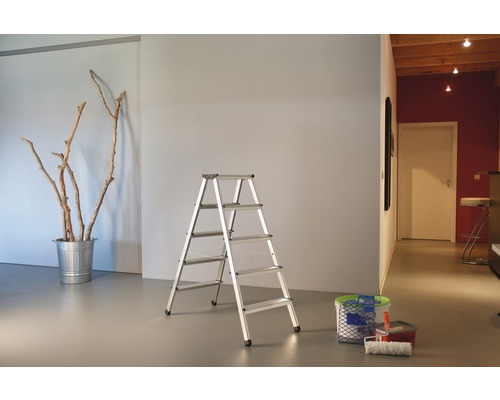 Rumsöversikt med en aluminiumstege, en hink med grenar och målningsredskap