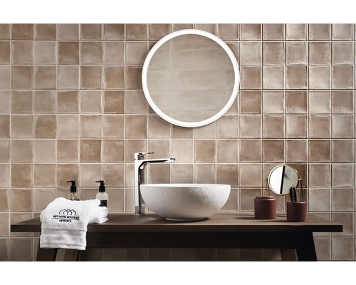 Ljust badrum med bruna plattor, rund spegel och modernt tvättställ