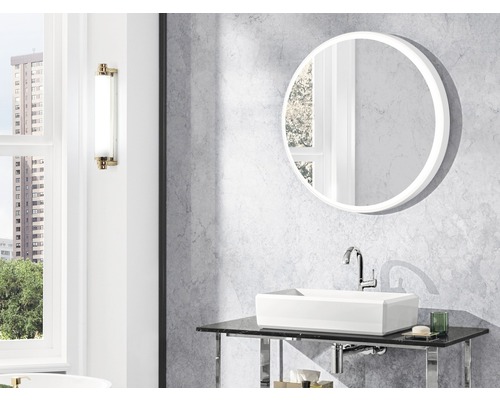 Badrum med rund spegel, tvättställ och vägglampa.