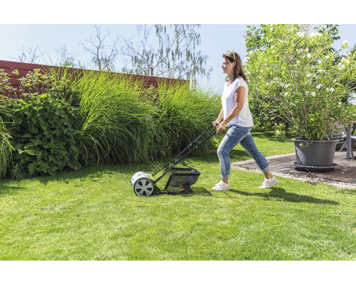 En kvinna använder en gräsmattluftare i trädgården för att underhålla gräsmattan.