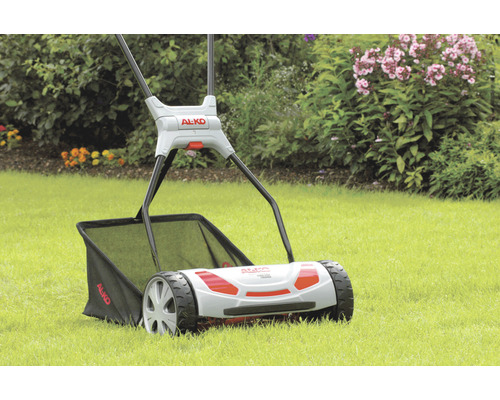 AL-KO vertikalskärare på gräsmatta med blommor i bakgrunden