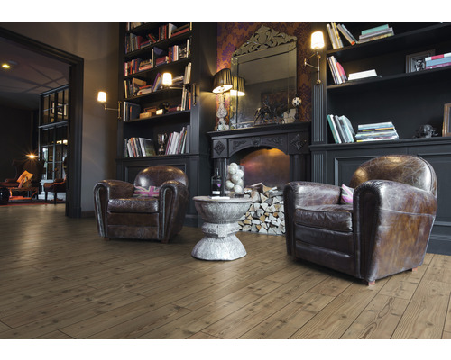 Vardagsrum med brunt trägolv, fåtöljer och öppen spis.