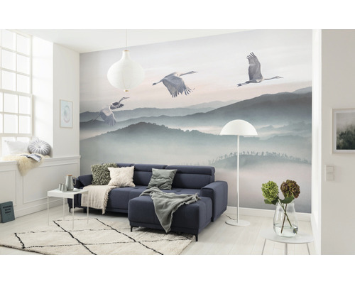 Vardagsrum med fototapet bergslandskap och tranor, soffa, matta och dekoration.