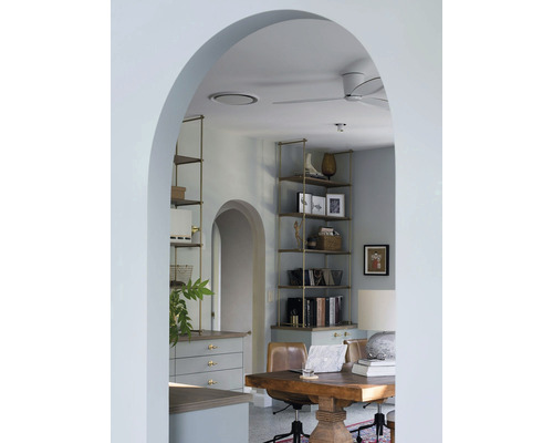Interiör av ett arbetsrum med skrivbord, hyllor och dekoration, fotograferat genom en välvd passage