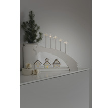 Dekorativ julscen med ljusbåge, stjärnljus, små hus och en krukväxt.